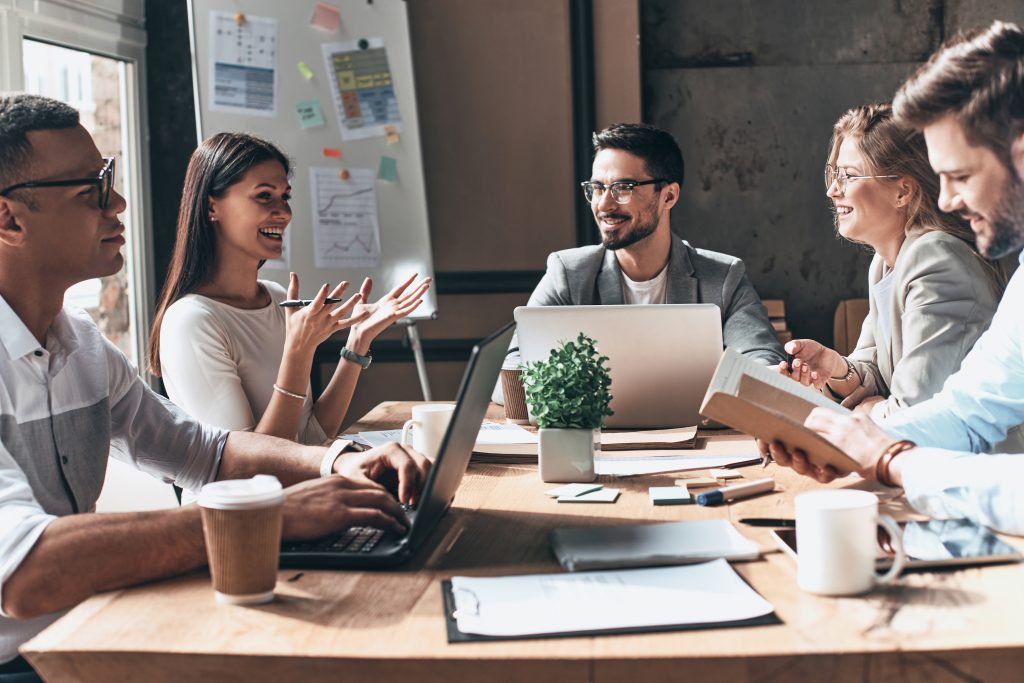 Working together. Group of young modern people in smart casual wear discussing business and smiling while sitting in the creative office