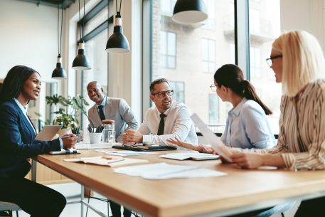 Group of diverse businesspeople smiling while discussing paperwork together during a meeting around a table in a modern office